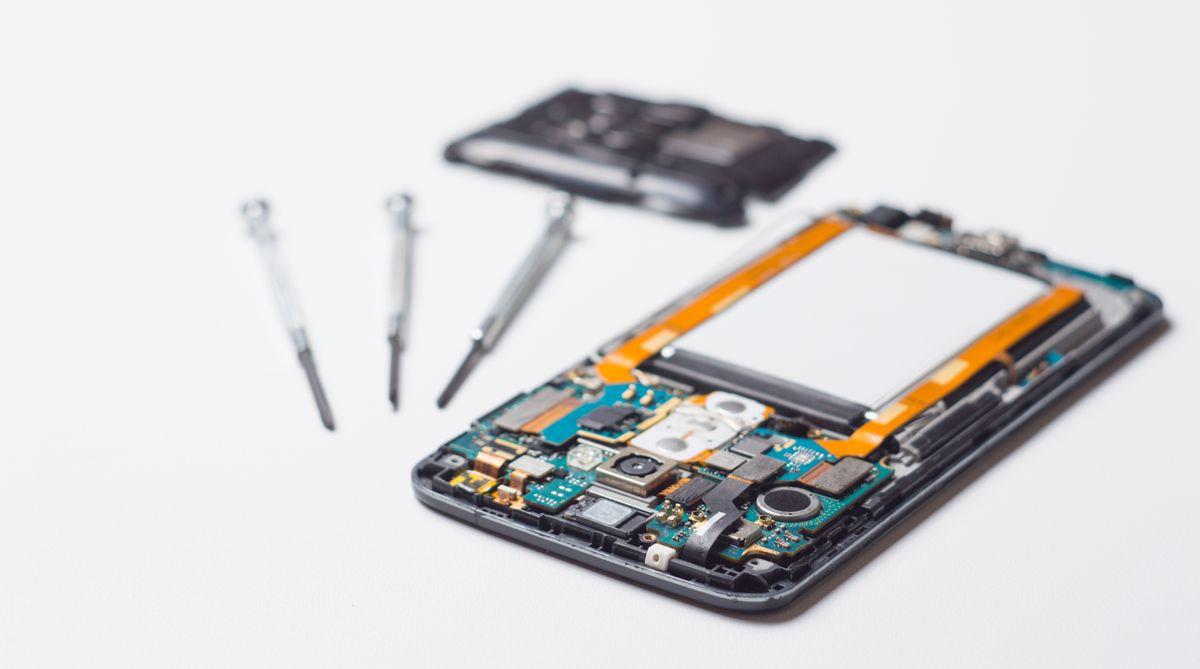 A process of mobile phone repairing and other gadgets parts of disassembled smartphone with screwdrivers on white table.